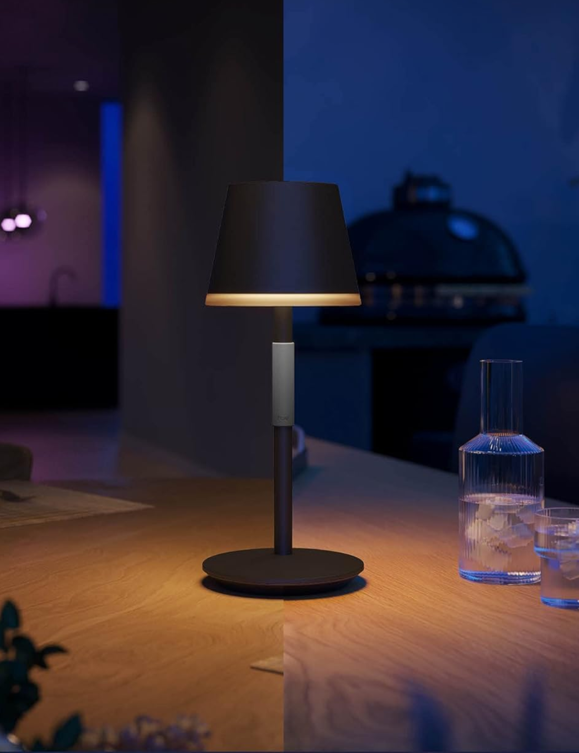 Style lampe de table portable PHILIPS Hue Go Smart sur une table de patio en bois à côté d'un ensemble de carafes cannelées