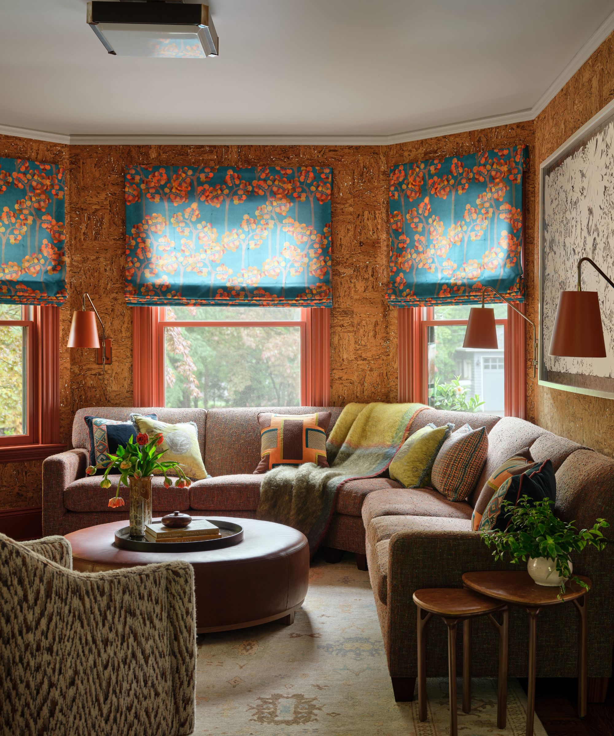 Salon confortable avec des murs en liège, un canapé sectionnel marron et des stores romains fleuris bleu sarcelle et orange.