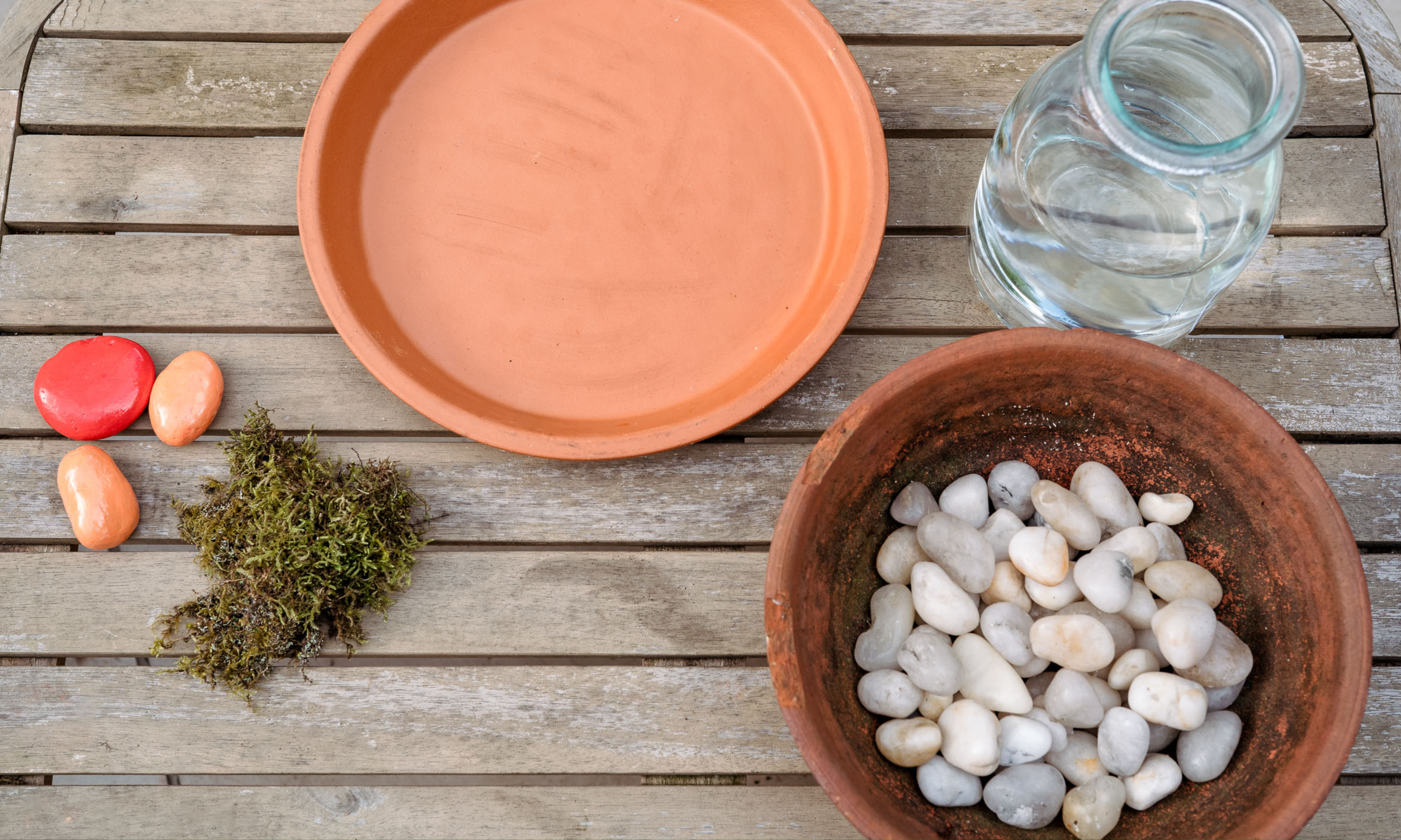 écorcher un vase en verre, des pierres blanches dans un arc rustique, une soucoupe en terre cuite, de la mousse et des pierres peintes